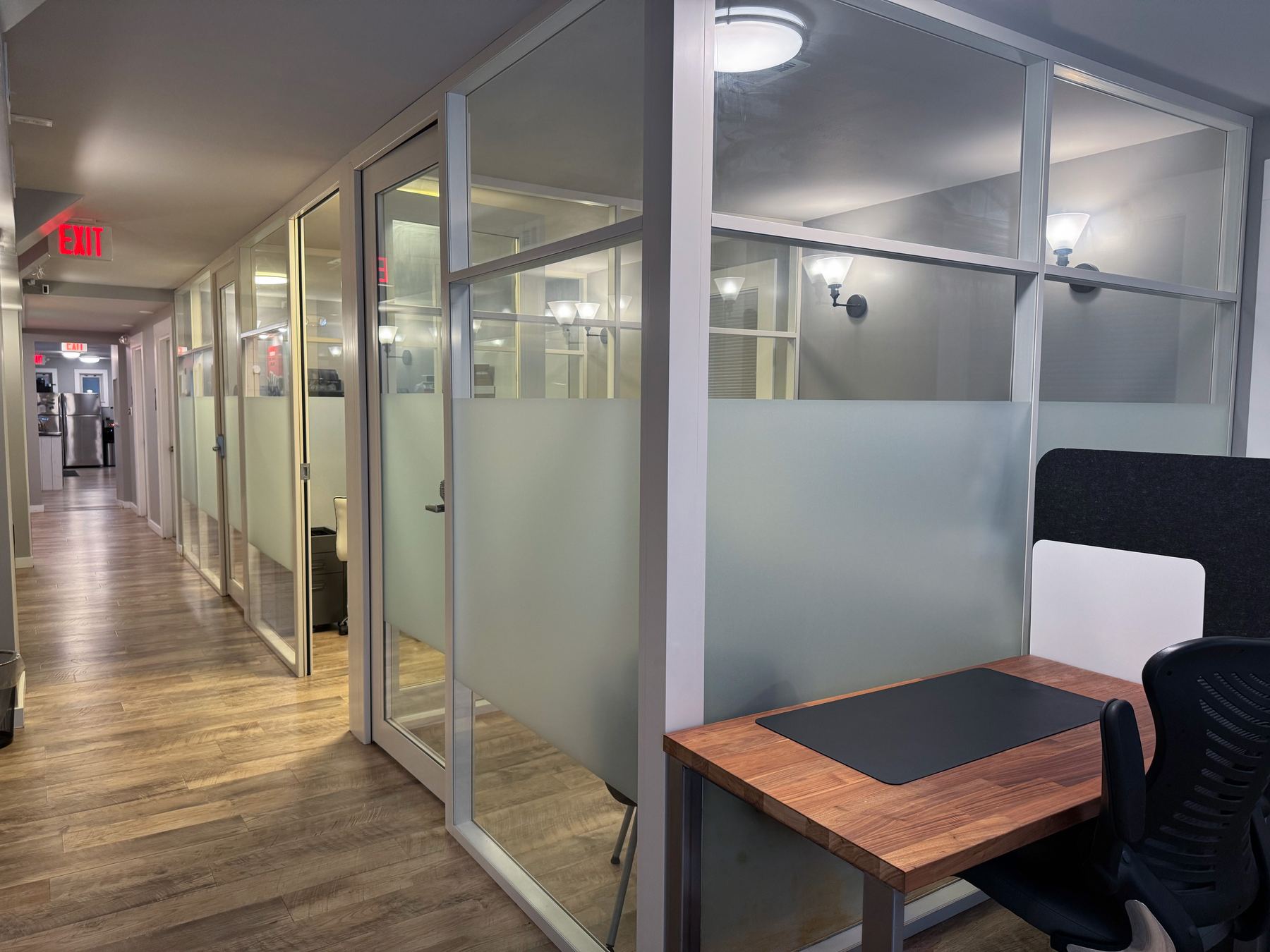 Hallway of glass private offices with frosted panels and wood floors
