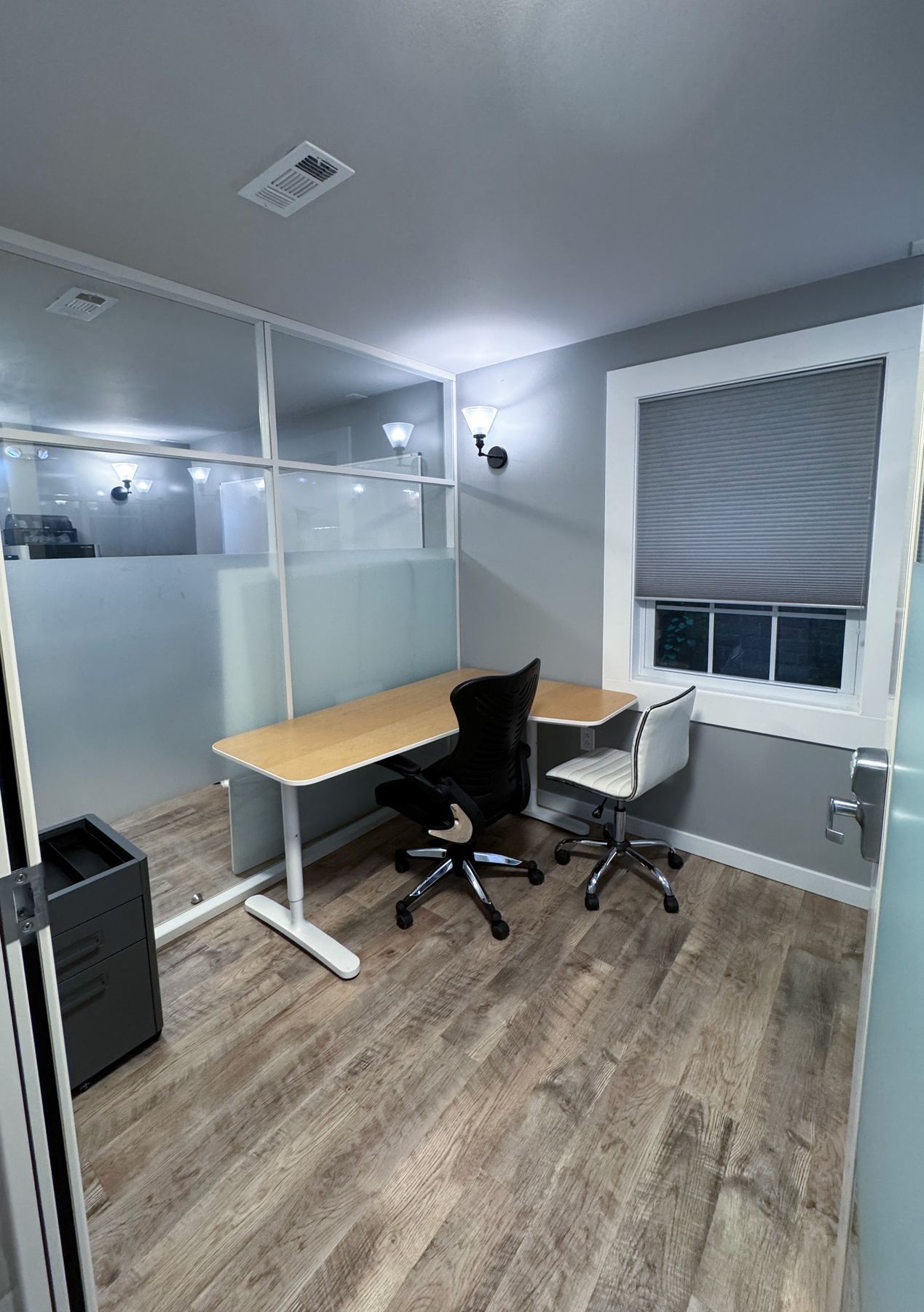 A lockable private office with a wood L-shaped desk, mesh chair, and frosted glass wall